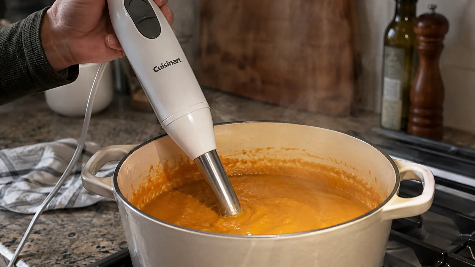 Hand-held immersion blender submerged in a pot of blended vegetable soup on a stovetop