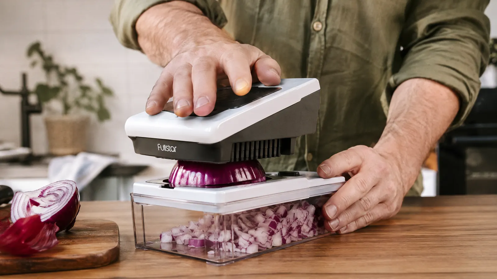 Hand pressing the lid of a white vegetable chopper down onto a whole onion with the collection container underneath