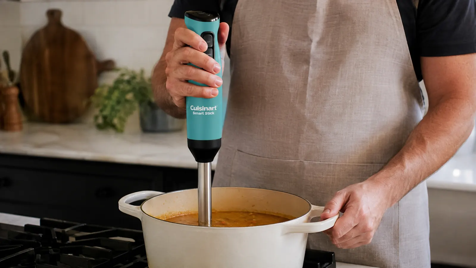 A hand holding the immersion blender directly in a pot, blending soup with the blending shaft submerged