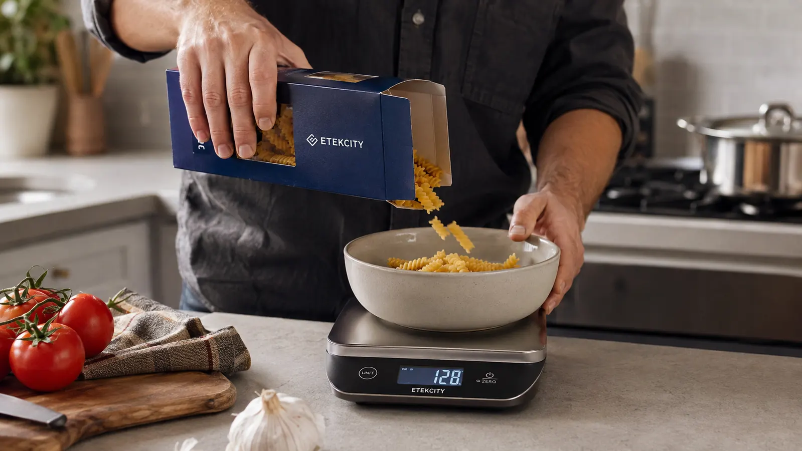 A hand tilting a box of pasta to pour into a bowl resting on the kitchen scale's platform with the display lit