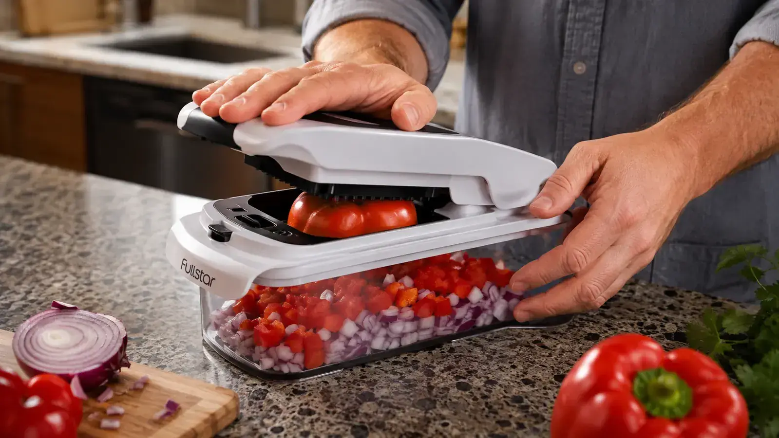 Hand pressing down on a white vegetable chopper over a stainless steel bowl filled with diced bell peppers and onion