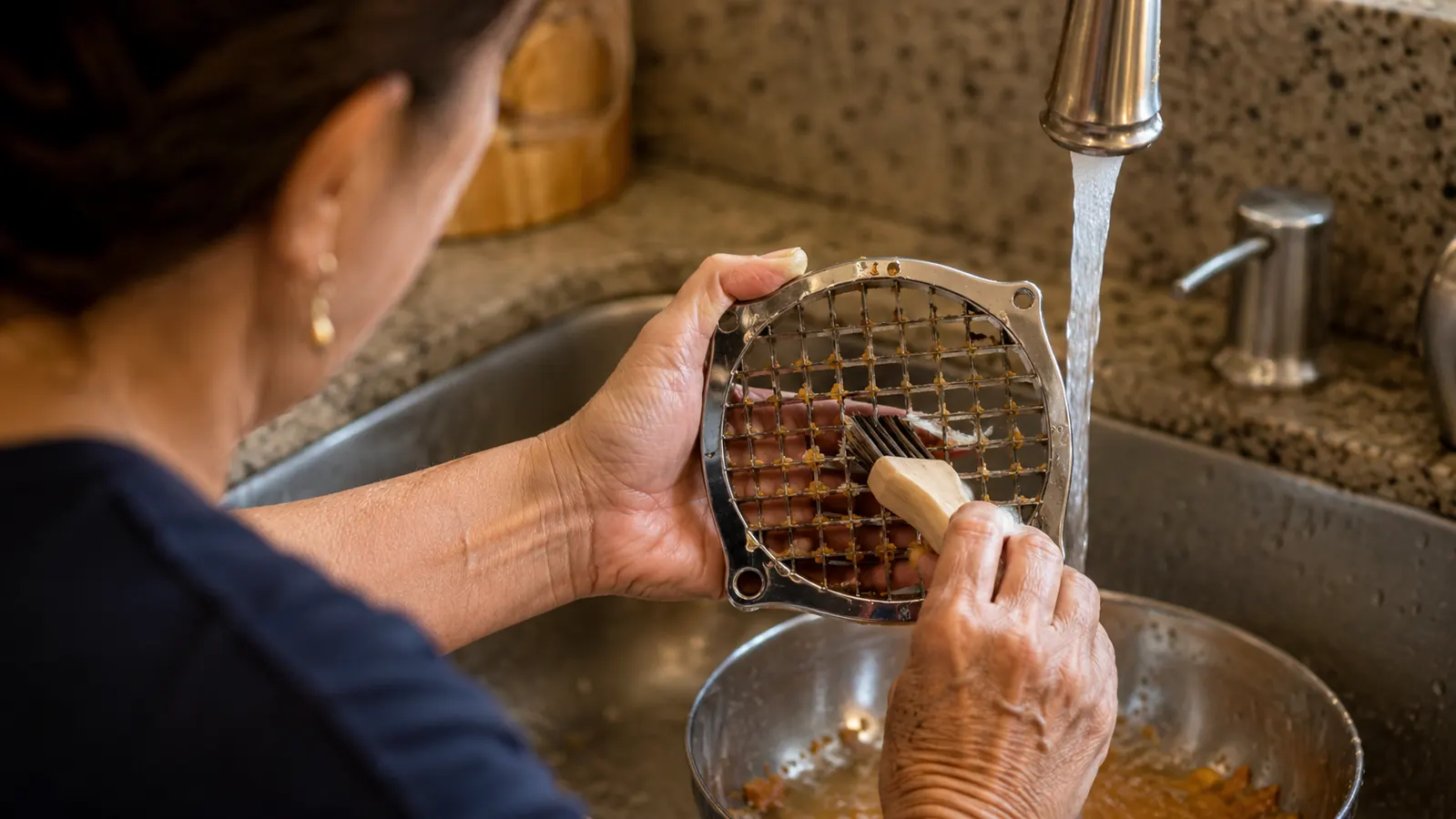 Close-up of a blade insert being cleaned with a small brush under running water in a kitchen sink