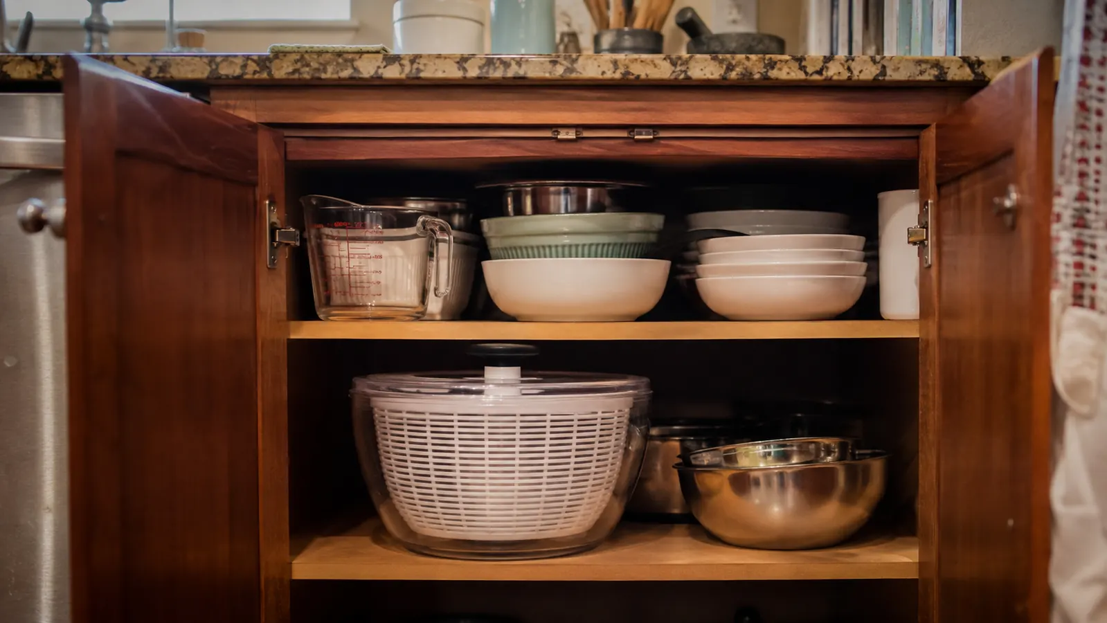 An open lower kitchen cabinet with the glass salad spinner taking up a large section of shelf space