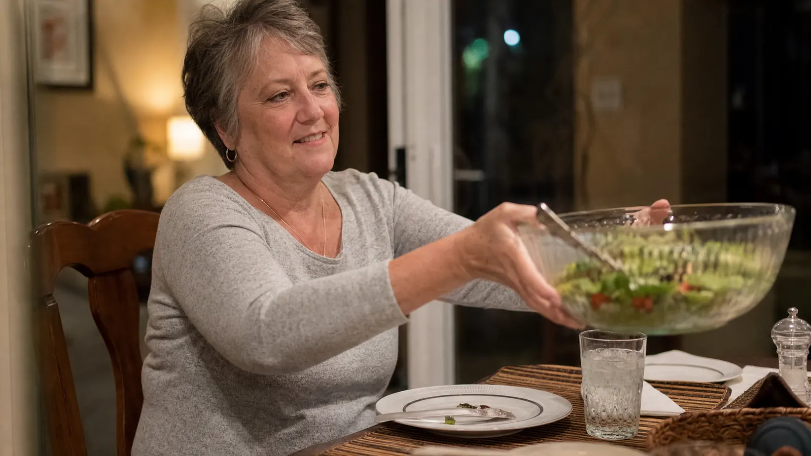 A family dinner table with a full salad bowl being passed between plates